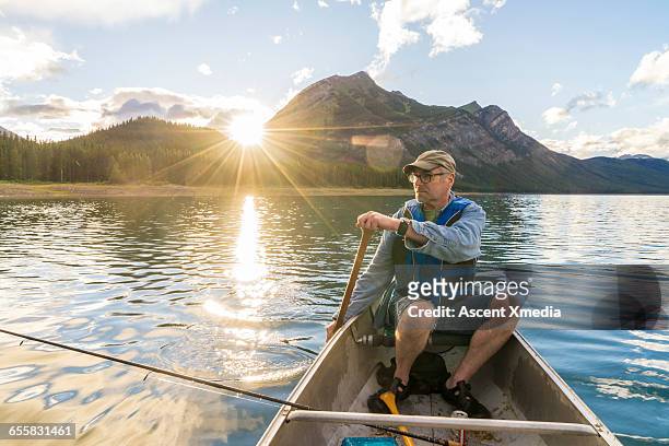 fisherman paddles canoe across tranquil mtn lake - mature men stock pictures, royalty-free photos & images