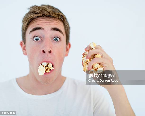a man with a bulging mouth full of popcorn - avidité photos et images de collection