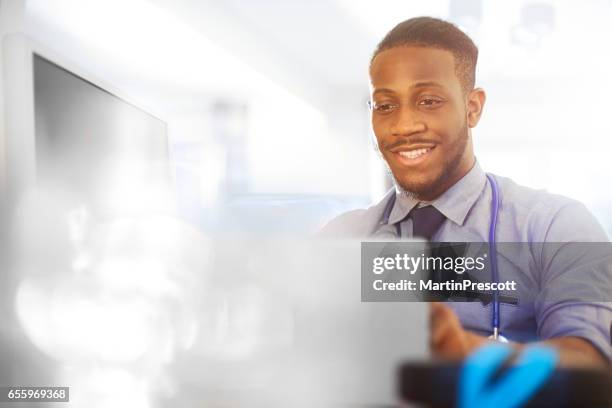 研修医が彼の机で彼の作品と笑顔 - ジュニアドクター ストックフォトと画像