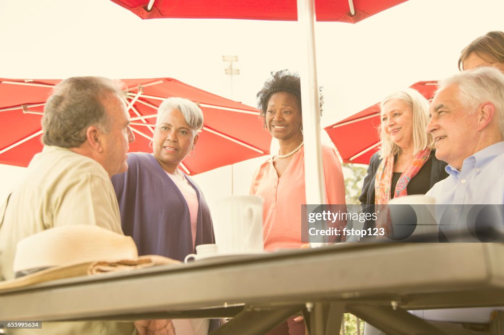 Multi-ethnic group of senior adult friends enjoy visiting at outdoor cafe.