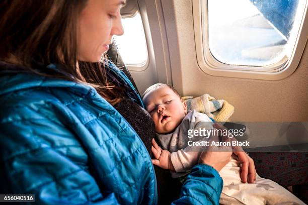 baby sleeps in mom's arms while on an airplane in flight. - black baby 個照片及圖片檔