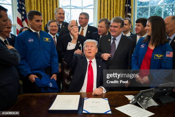 President Donald Trump hands out pens after signing the NASA transition authorization act in the Oval Office of the White House March 21, 2017 in...