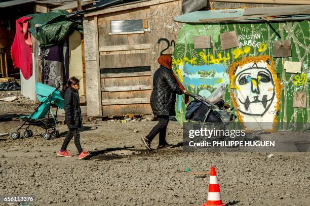 An Iraqi Kurds migrant woman followed by a girl carries kitchen ware in La Liniere camp in Grande-Synthe, northern France, on March 21, 2017. The...