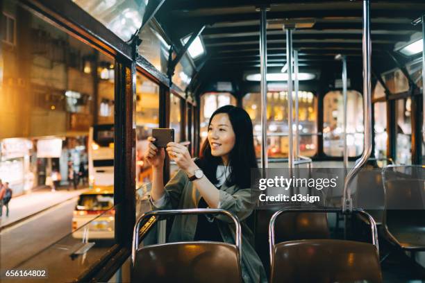 smiling female tourist taking pictures of night scene with smartphone on a tram ride in hong kong - hong kong travel stock pictures, royalty-free photos & images