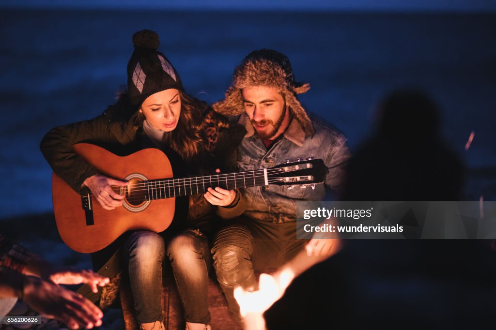 Friends playing guitar and singing at beach party at night