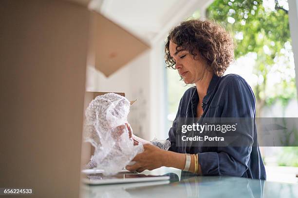 woman is wrapping object while sitting at table - bubble wrap stock pictures, royalty-free photos & images