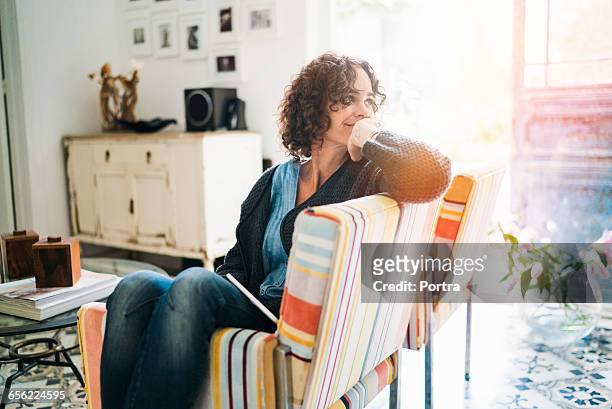 thoughtful woman sitting on chair at home - tevreden stockfoto's en -beelden