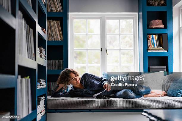 woman is reading magazine while lying on sofa - reading magazine stock pictures, royalty-free photos & images