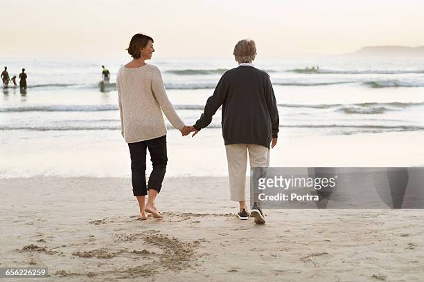 mother and daughter holding hands against sea - mature woman daughter stockfoto's en -beelden