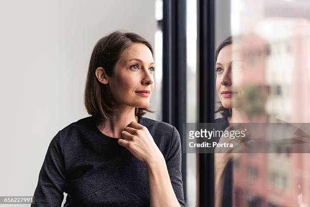 thoughtful businesswoman looking through window - reflection photos et images de collection