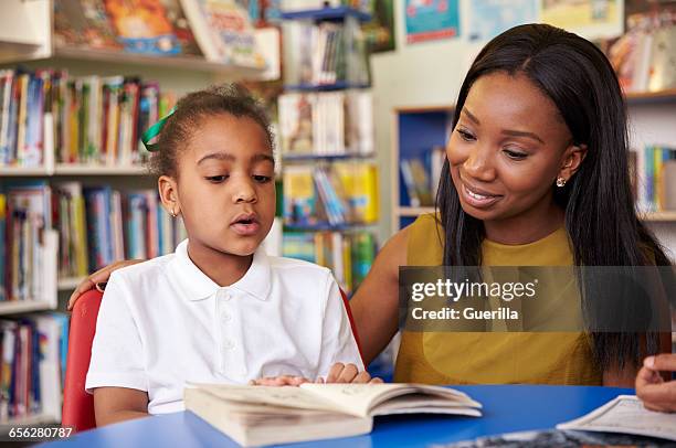 elementary school pupil reading in library with teacher - african american school uniform stock pictures, royalty-free photos & images