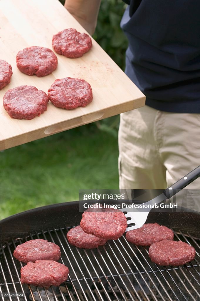 Man placing raw burgers on barbecue grill rack