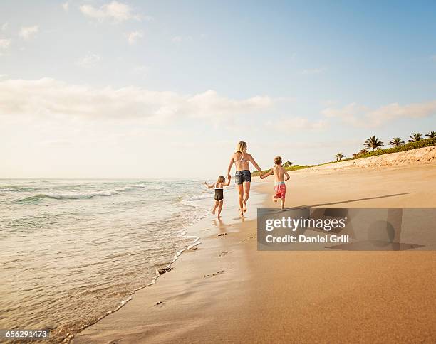 usa, florida, jupiter, mother running with boy (6-7) and girl (4-5) on beach by water - jupiter florida stock pictures, royalty-free photos & images