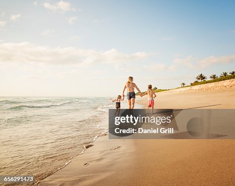 USA, Florida, Jupiter, Mother running with boy (6-7) and girl (4-5) on beach by water USA, Florida, Jupiter, Mother running with boy (6-7) and girl (4-5) on beach by water