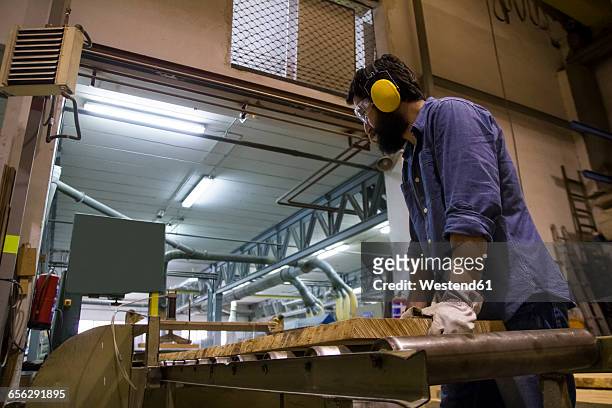 craftsman with hearing protection, gloves and safety glasses using an industrial circular saw in a factory - depósito de madeiras imagens e fotografias de stock