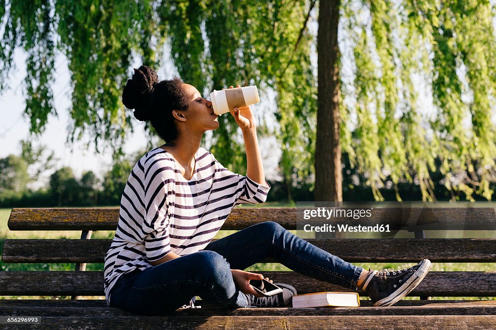Young woman sitting on park bench drinking coffee to go