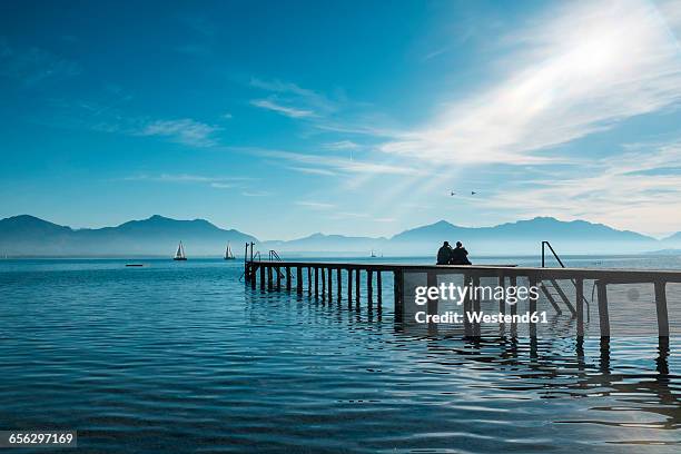 germany, lake chiemsee, seebruck, two people on wooden jetty - bayern menschen stock-fotos und bilder