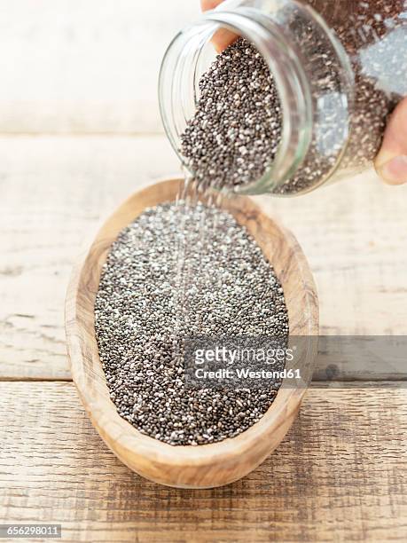 chia seeds being poured into a wooden bowl - chiasamen stock-fotos und bilder