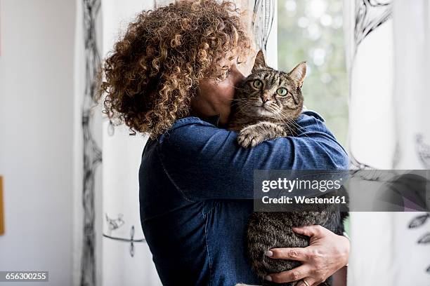 woman cuddling with cat by the window - cat cuddle stockfoto's en -beelden