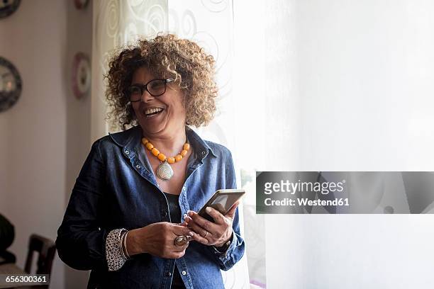 laughing woman holding phablet by the window - 50 54 years stock pictures, royalty-free photos & images