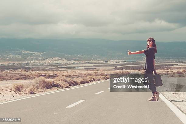 young woman with suitcase hitchhiking on road - hitchhiking 個照片及圖片檔