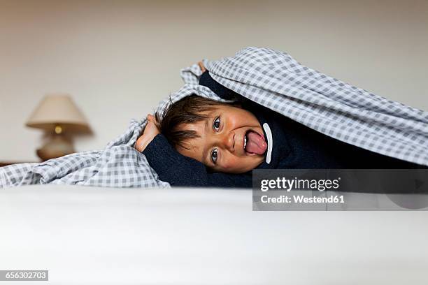 little boy lying under the blanket on his bed sticking tongue out - under tongue stock pictures, royalty-free photos & images