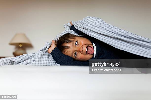 little boy lying under the blanket on his bed sticking tongue out - under tongue 個照片及圖片檔