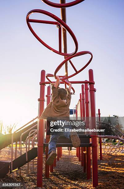 rear view of boy swinging on monkey bars in playground - monkey bars fotografías e imágenes de stock