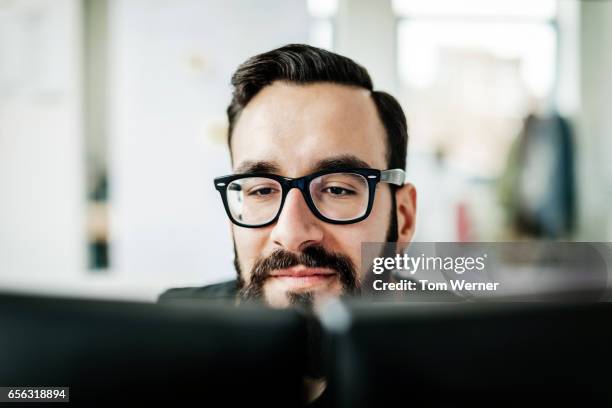 young latin businessman looking at his computer monitors - southern european descent stock pictures, royalty-free photos & images