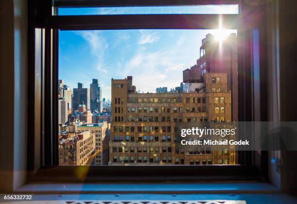 looking through a window toward colorful view of midtown manhattan with rooftops and water towers against a bright blue sky - nyc building sun ストックフォトと画像