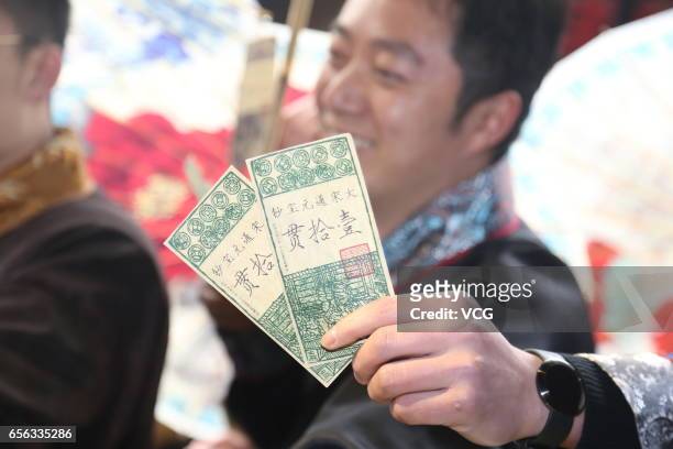 Staff dressed in ancient costume receive ancient paper currency as his bonus at Hangzhou Songcheng scenic spot on March 22, 2017 in Hangzhou,...