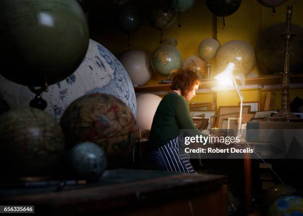 globe maker examining small globe in workshop - desk lamp fotografías e imágenes de stock