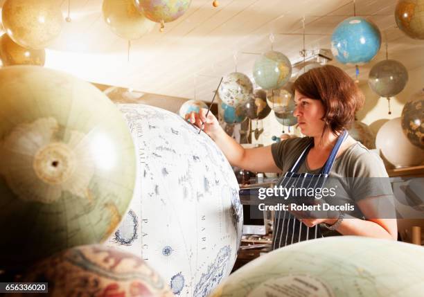 female globe maker applying detail by hand to large globe - cartograaf stockfoto's en -beelden