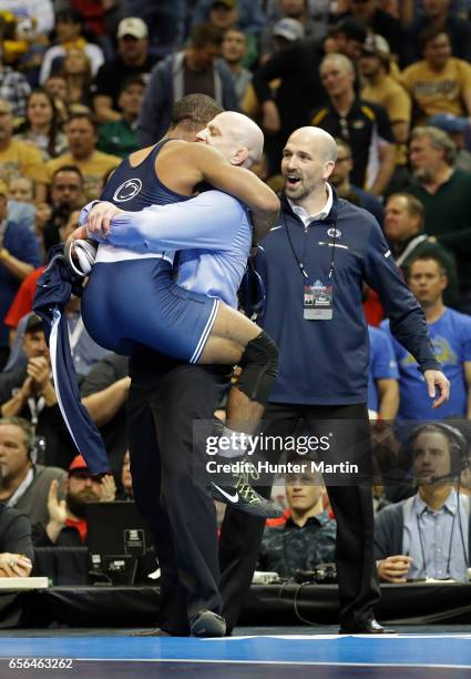 Mark Hall of the Penn State Nittany Lions jumps into the arms of head coach Cael Sanderson as assistant coach Casey Cunningham looks on after winning...