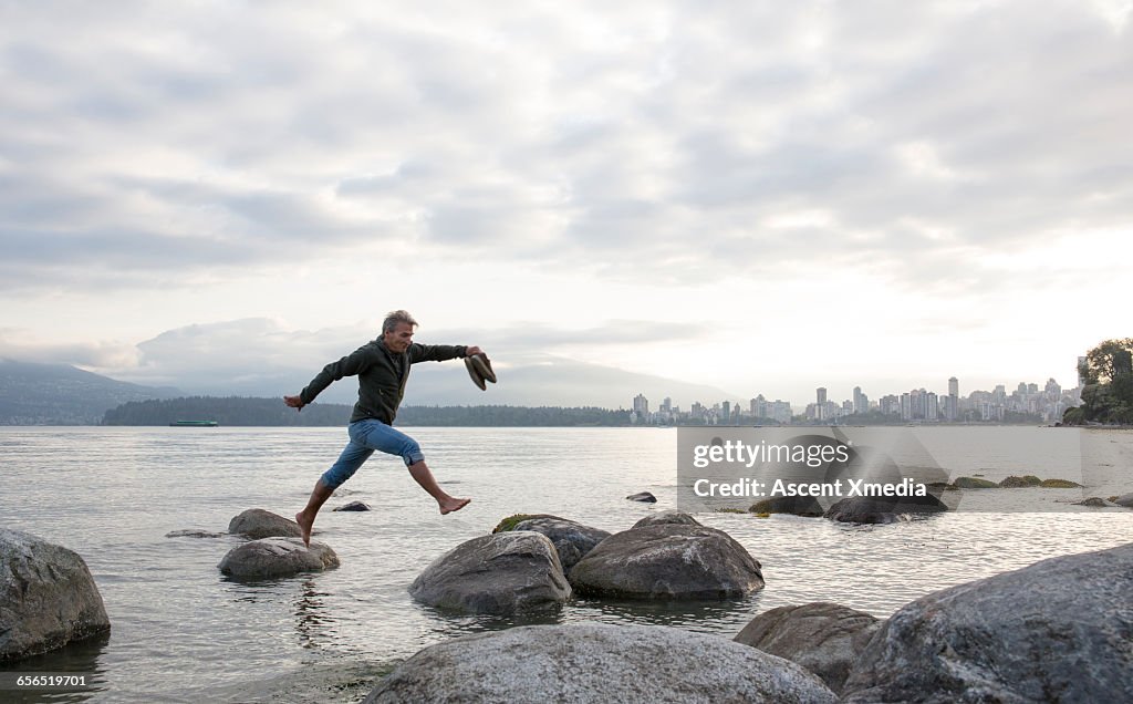 Man leaps across gap between rocks, city behind