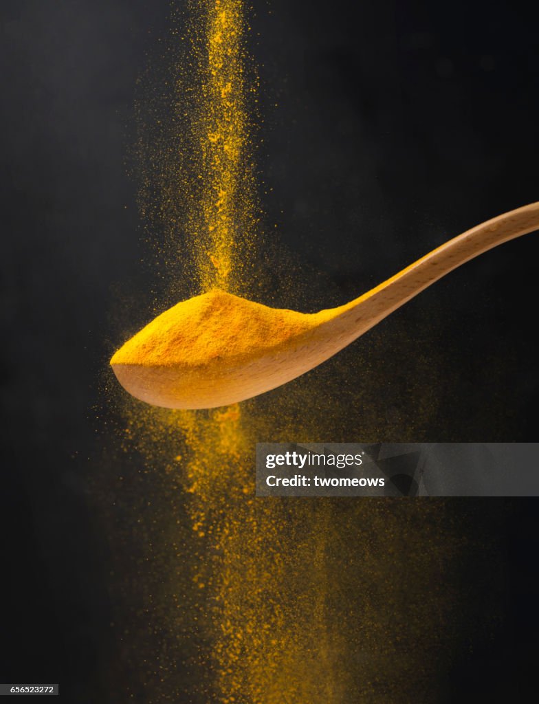 Close up view of turmeric powder in wooden spoon.