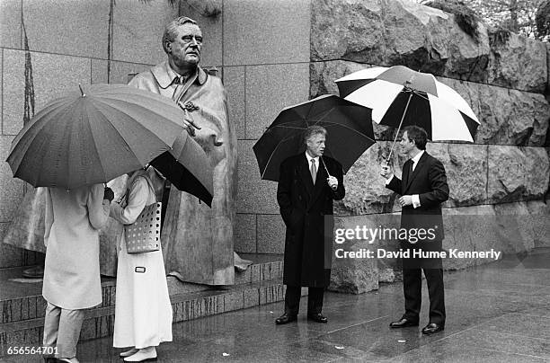 First Lady Hillary Clinton and Cherie Blair, the wife of British Prime Minister Tony Blair, chat under umbrellas to the left while U.S. President...