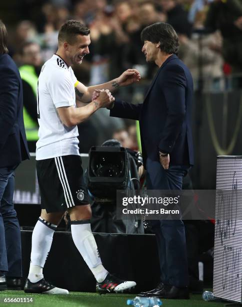 Lukas Podolski of Germany shakes hands with Joachim Loew, manager of Germany as he is subbed during his last international match for Germany during...