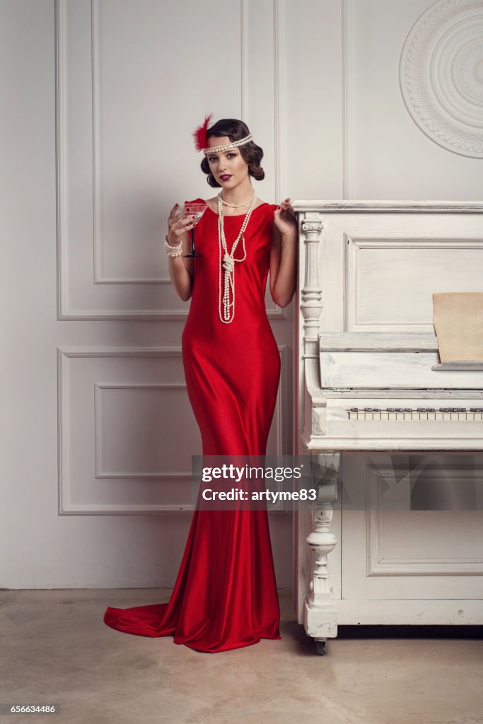 Joven Hermosa Chica En Vestido Rojo Estilo Años 20 O Años 30 Con Vidrio De Martini Cerca Del Piano Hermosa Mujer De Estilo Vintage Old Fashioned Peinado Onda Dedo Maquillaje Y Retro Joven Hermosa Chica En Vestido Rojo Estilo Años 20 O Años 30 Con Vidrio De Martini Cerca Del Piano Hermosa Mujer De Estilo Vintage Old Fashioned Peinado Onda Dedo Maquillaje Y Retro