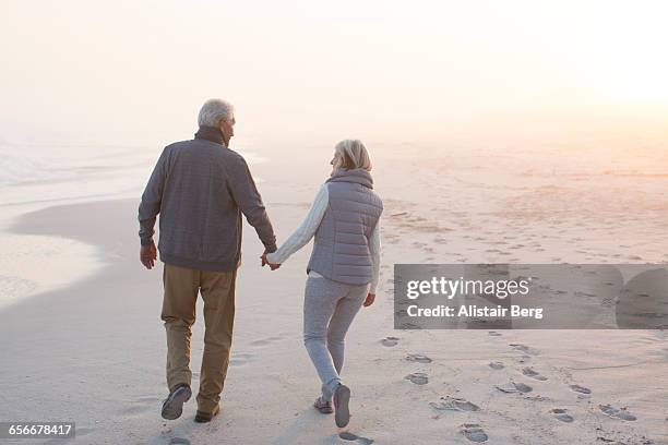 senior couple walking on a beach together - cardigan photos et images de collection