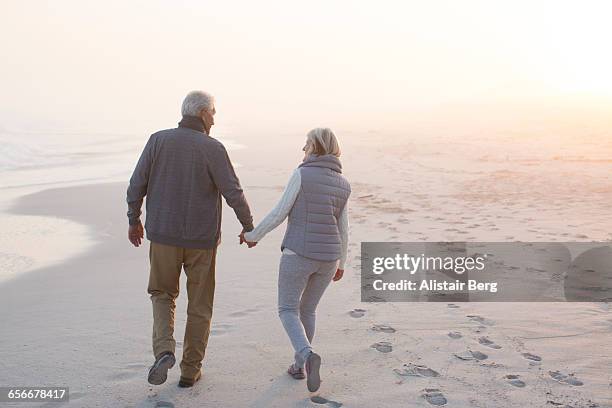 senior couple walking on a beach together - sweater vest stockfoto's en -beelden