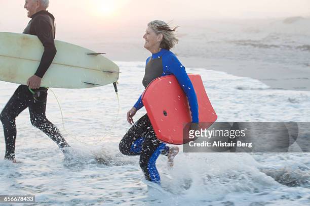 Senior couple running into sea with surf boards
