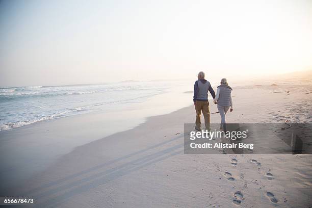 senior couple walking on a beach together - senior couple stock pictures, royalty-free photos & images