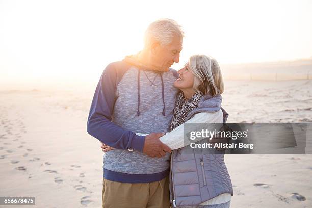 senior couple embracing on a beach together - active seniors beach stock pictures, royalty-free photos & images