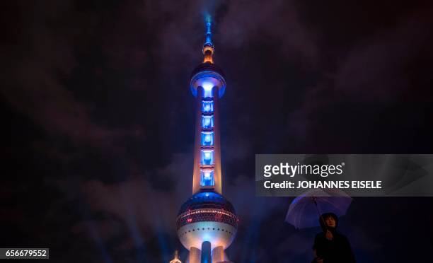 This picture taken on March 22, 2017 shows a woman holding an umbrella as she walks passed the Pearl Tower in Shanghai. / AFP PHOTO / Johannes EISELE