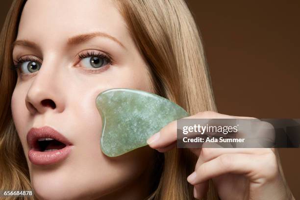 beautiful woman with jade massaging stone on her cheek - jade gemstone stockfoto's en -beelden