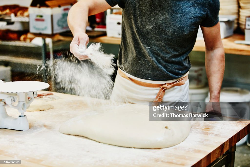Baker spreading flour on dough in commercial bakery