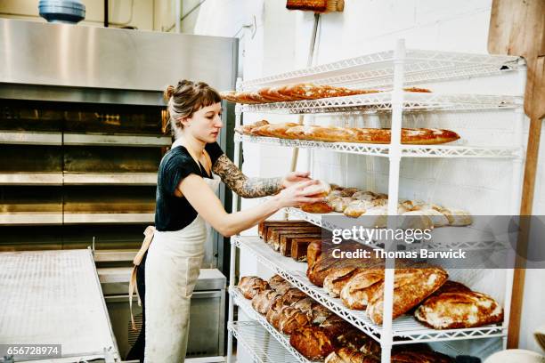 female baker placing bread fresh from oven on cooling rack - america patisserie fotografías e imágenes de stock