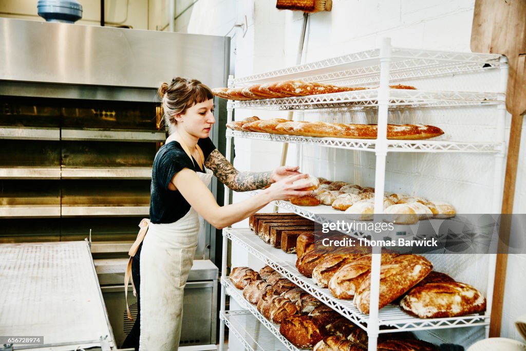 Female baker placing bread fresh from oven on cooling rack