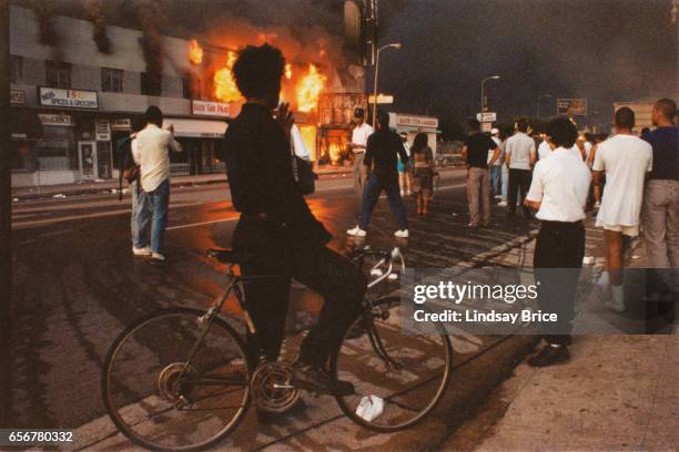 Rodney King Riot. A view of businesses beginning to burn on Pico Boulevard near Hayworth Avenue, onlookers gathering, a young man dressed in black...